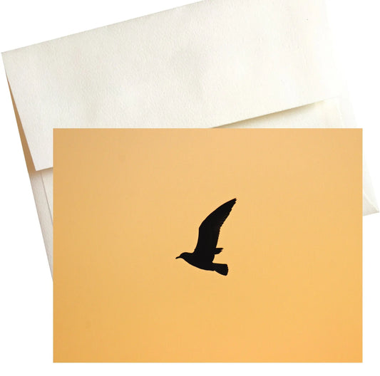 A photo of a lone gull soaring gracefully against a breathtaking golden sunset sky. The warm yellow hues create a dramatic backdrop for the dark silhouette of the gull, its wings outstretched as it flies towards the horizon.