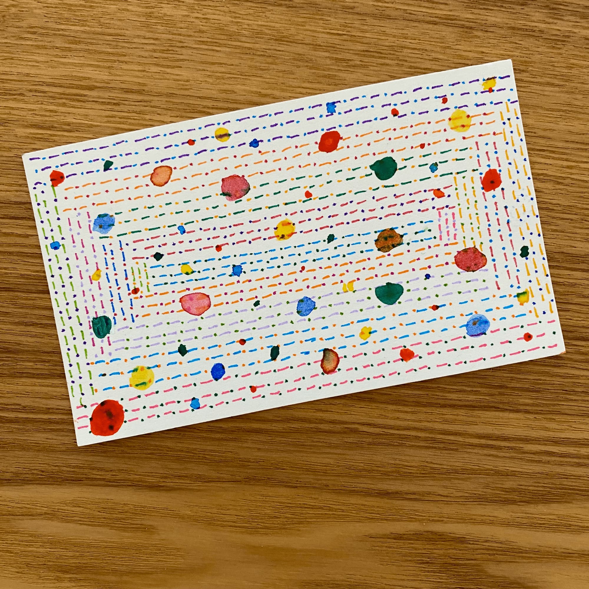 abstract sketch on index card with multicolor dashes fillng up the rectangle of the card and topped with multicolor watercolor dots