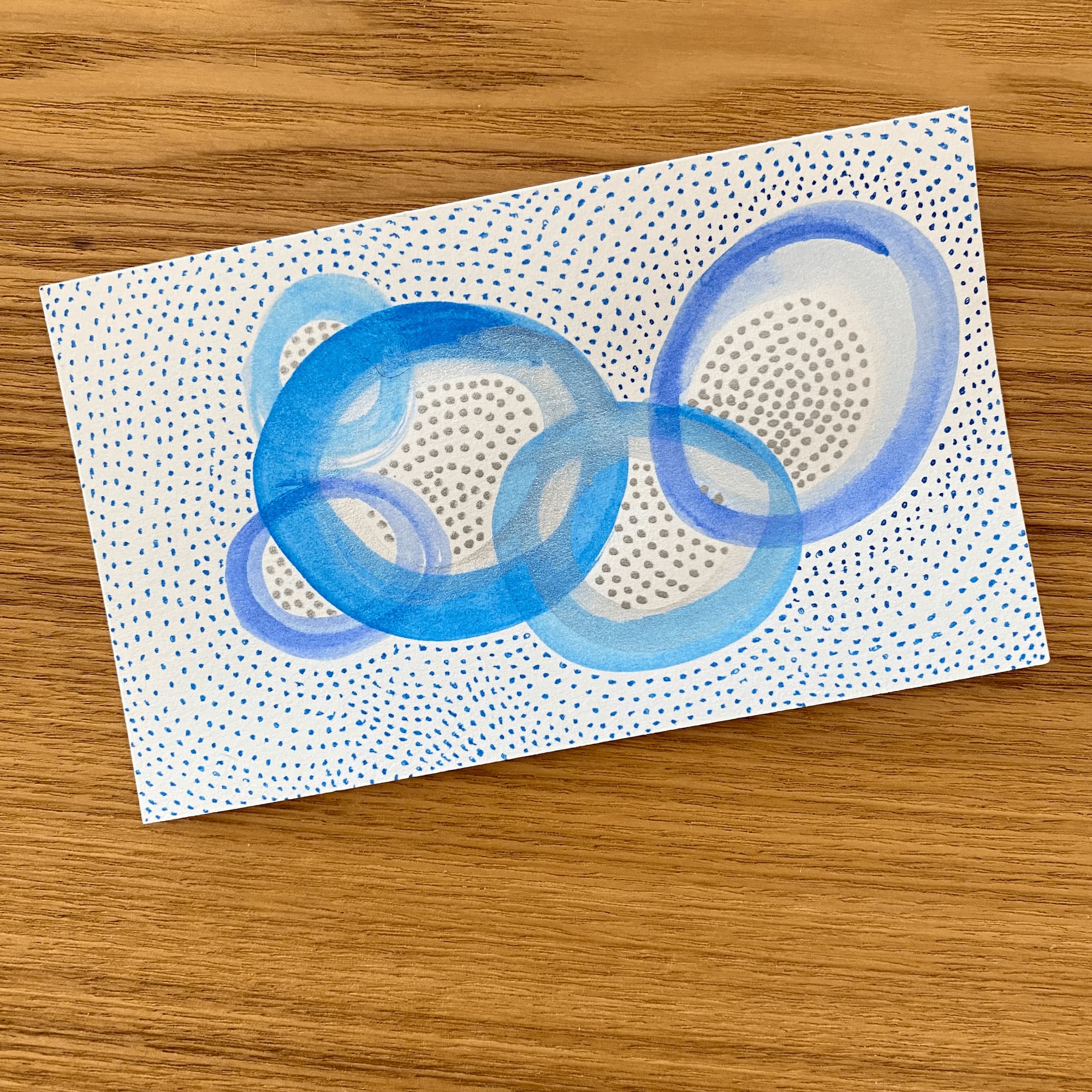 abstract painting of circles and dashes done in shades of blue and silver.