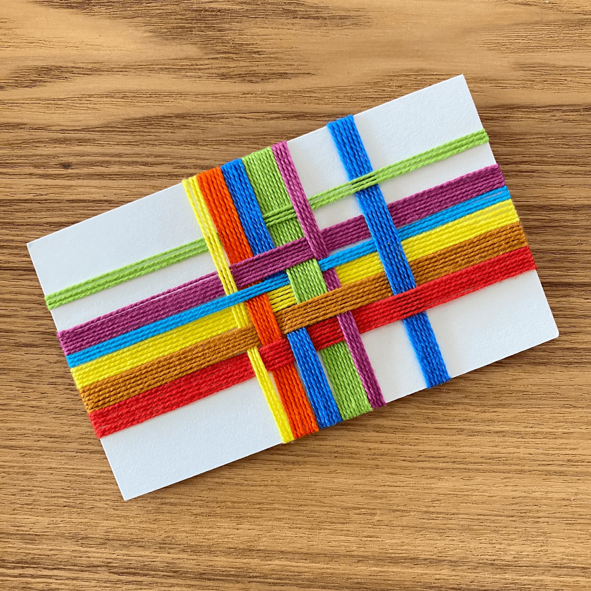index card with a fiber art plaid made with overlappiing colored cotton cord