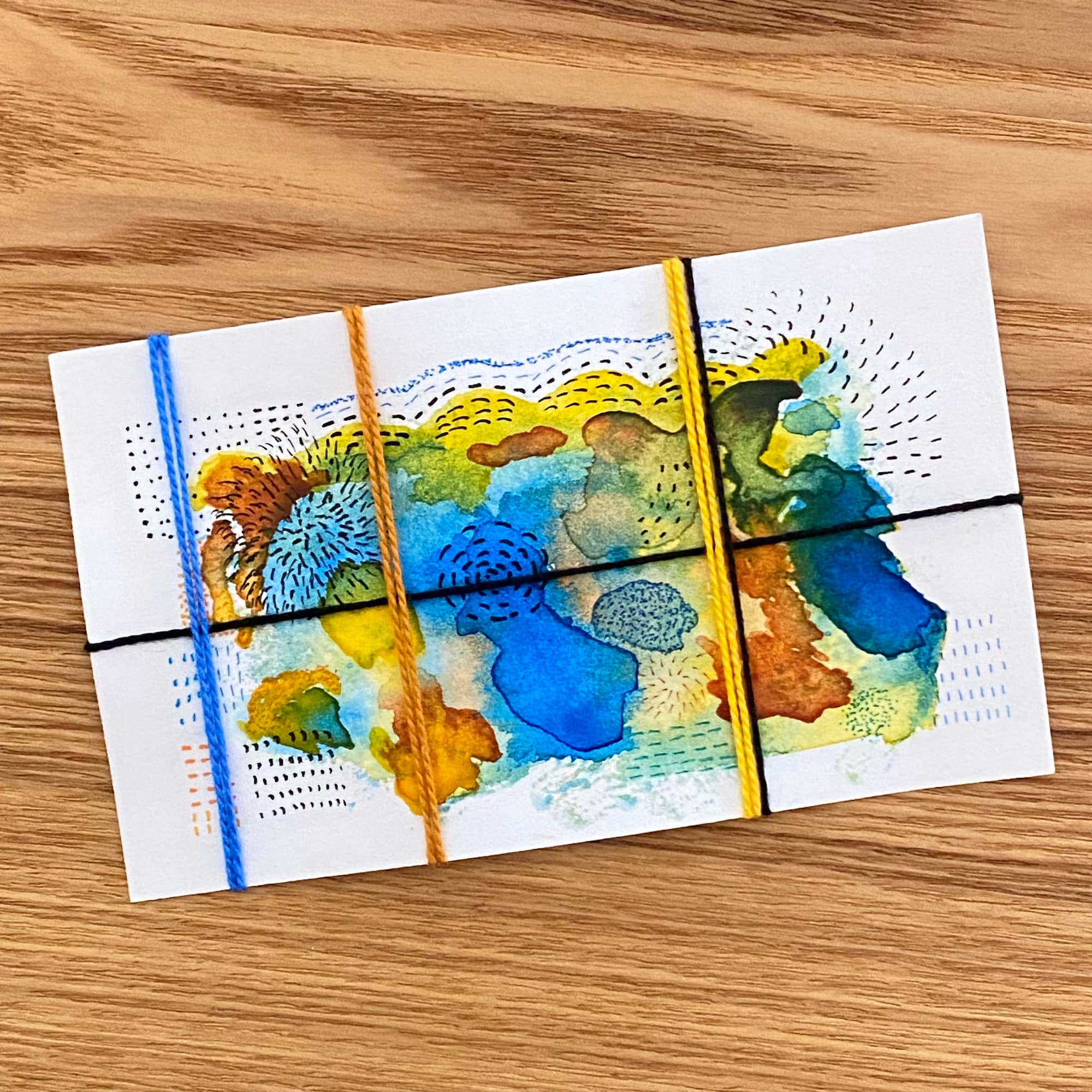 abstract watercolor in blue, bronze and yellow with ink markings and cotton cord in the same colors