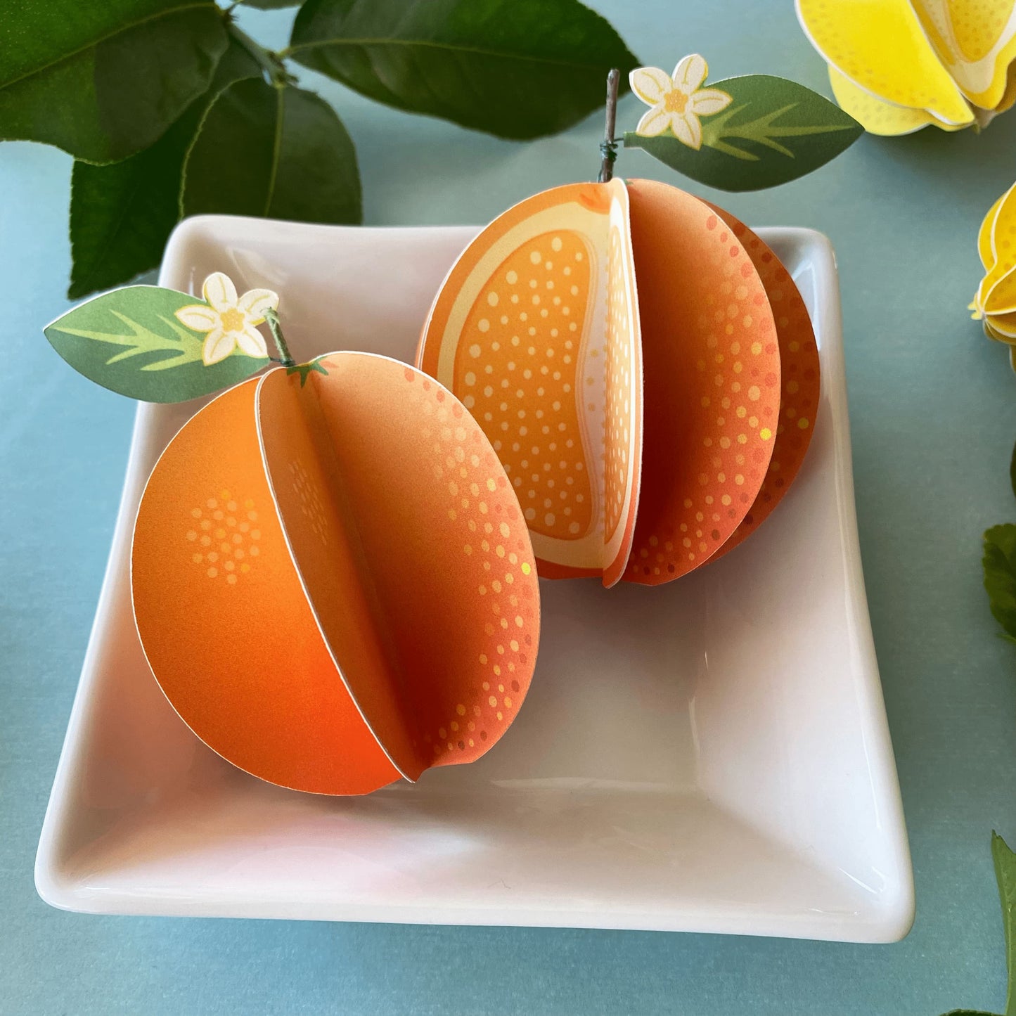 a set of 2 paper oranges, one whole and one cut, in a small white dish