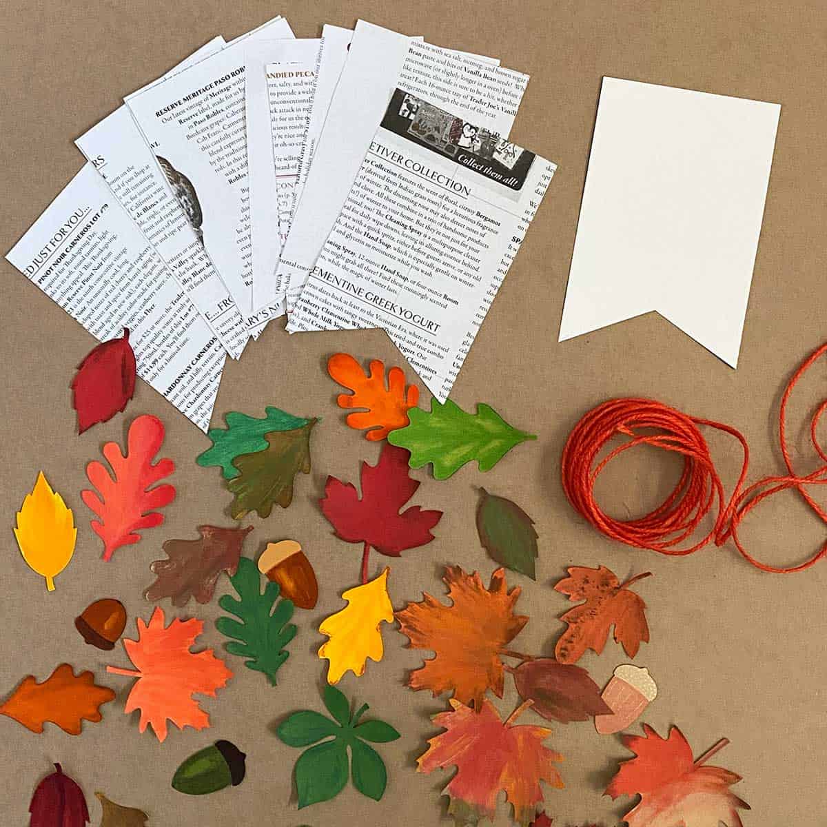 Various handprinted leaves with newsprint  pennants and orange twine for a leaf banner tutorial for Cakewalk DIY.