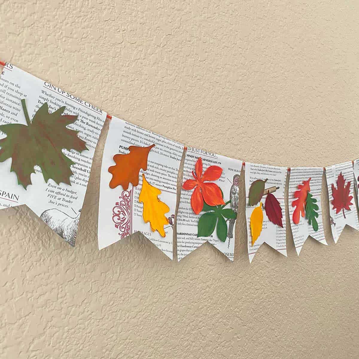 banner of handprinted leaves on pennants hanging across a wall to showcase a tutorial for CakewalkDIY.