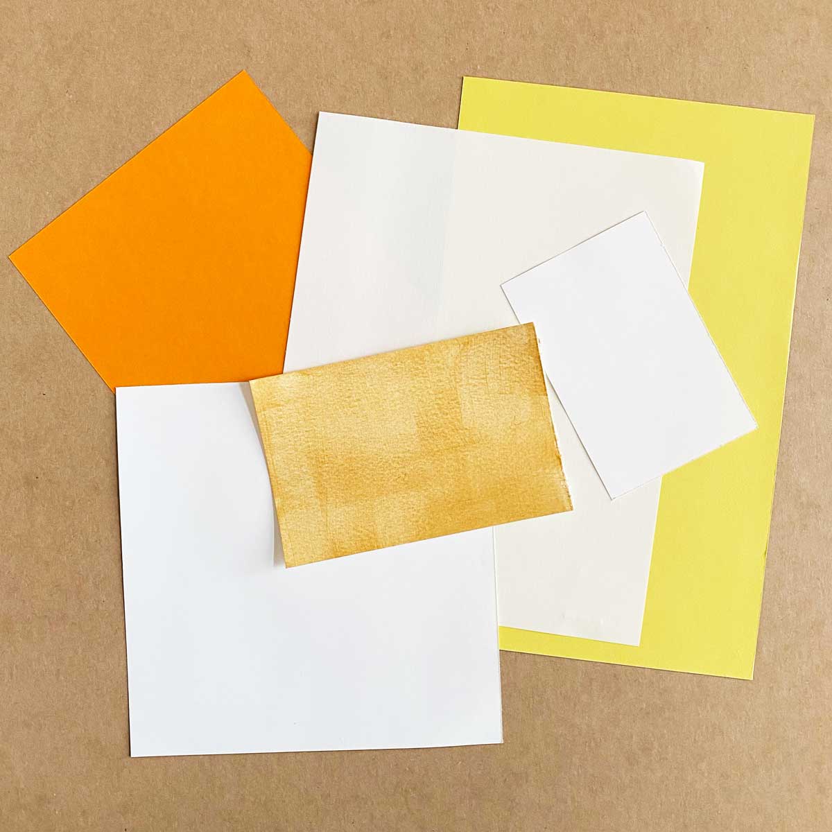 Assorted colored paper sheets and mat board on a brown background for a Cakewalk DIY Paper Craft tutorial