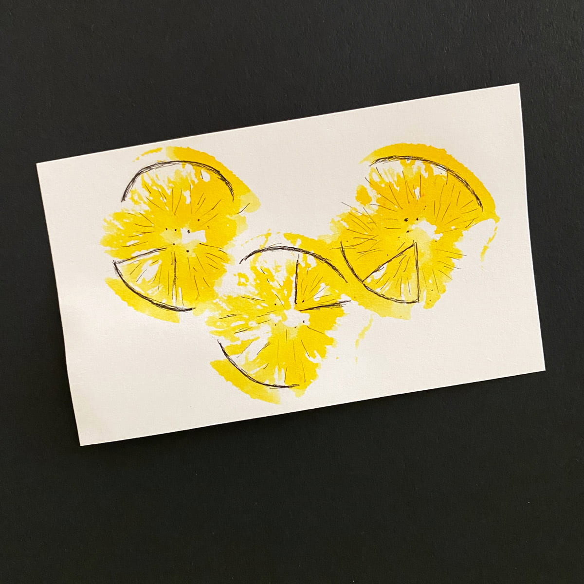 Index card with a lemon stamp and ink with pen detailing of a lemon imprint in yellow and black on a black background by Mozaic Studio for ICAD 2025.
