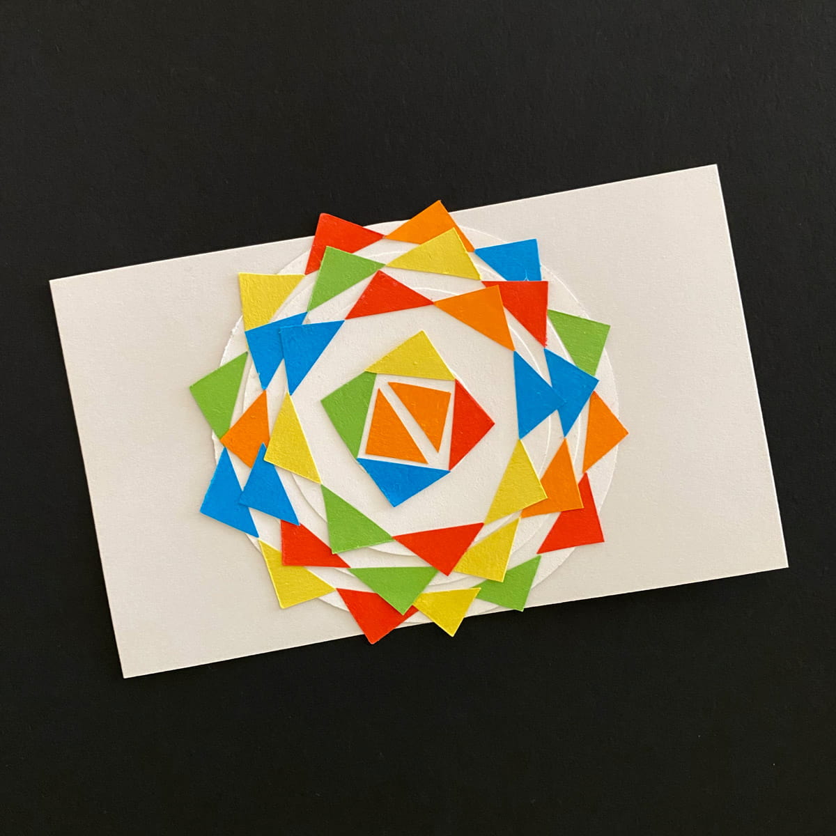 Index card with collage of white paper circles and triangles in yellow, blue, red and green on a black background by Mozaic Studio for ICAD 2025