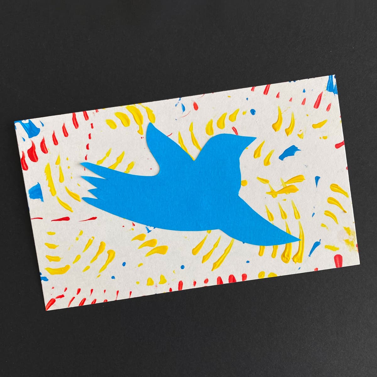 Index card with a collage of a bird silhouette in bright blue colored paper on a background of acrylic paint strokes in bright blue red and yellow on a black background by Mozaic Studio for ICAD 2025