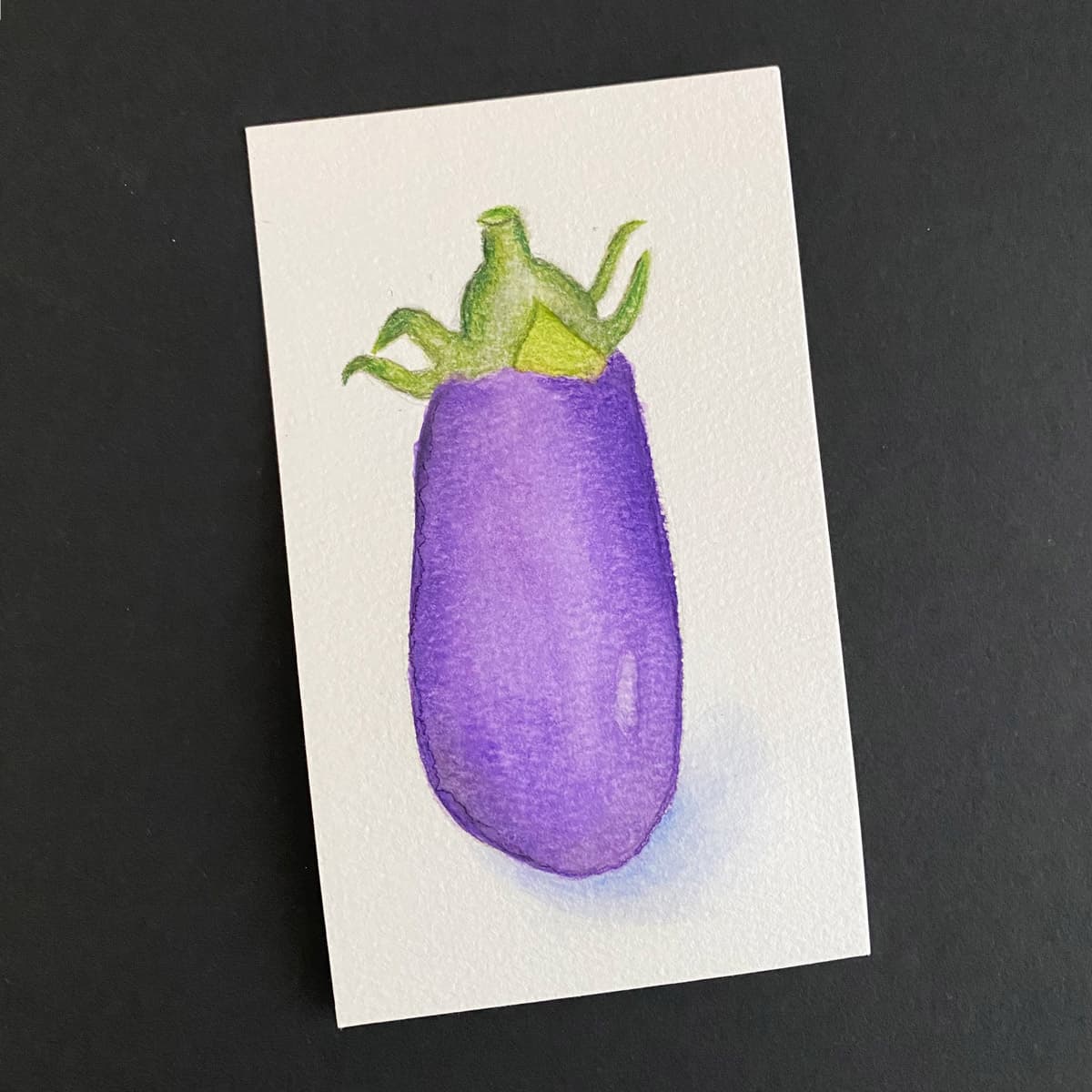 Index card with an eggplant painted in watercolors on a black background by Mozaic Studio for ICAD 2025