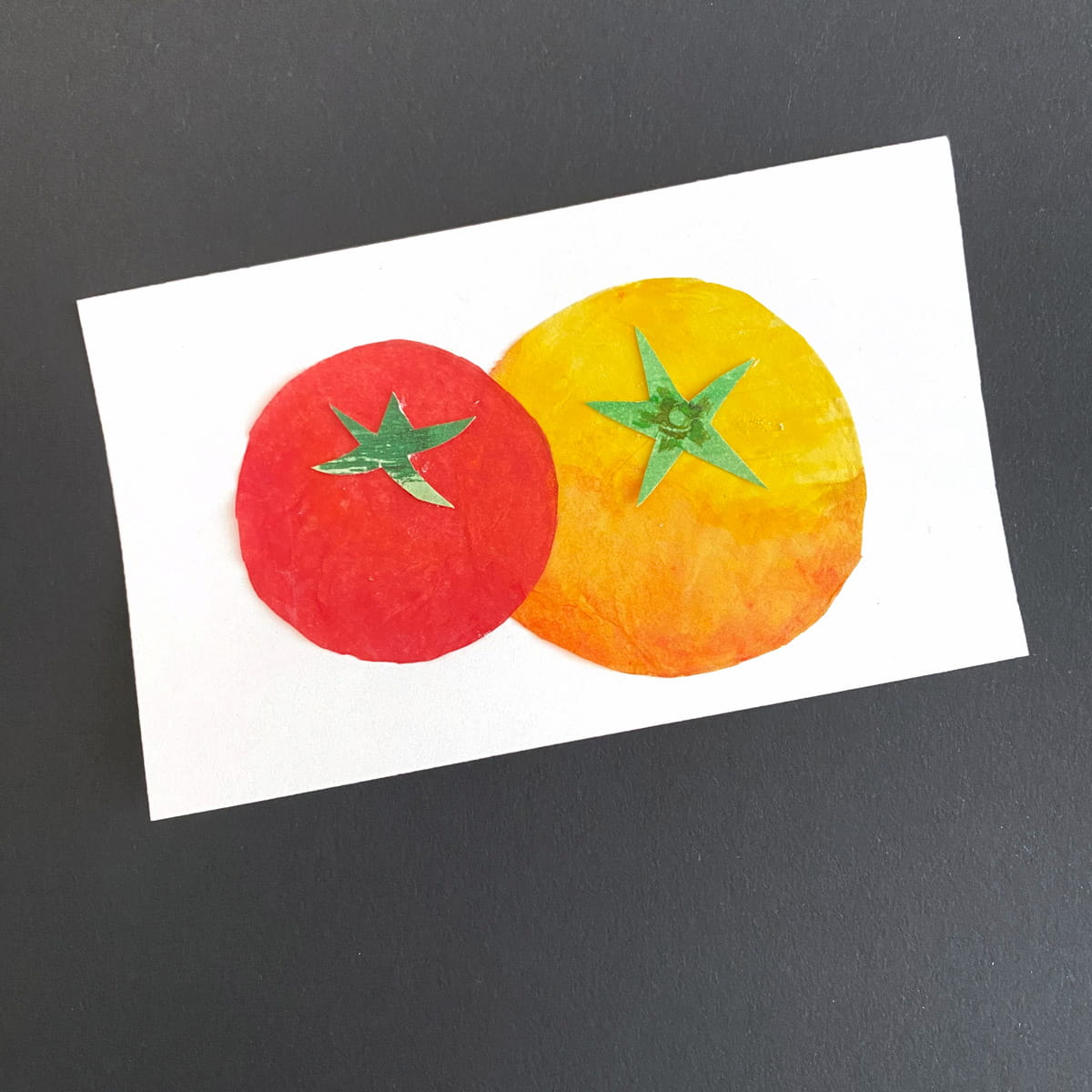 Index card with a a red and yellow tomato made from colored tissue paper and watercolor on a black background by Mozaic Studio for ICAD 2025.