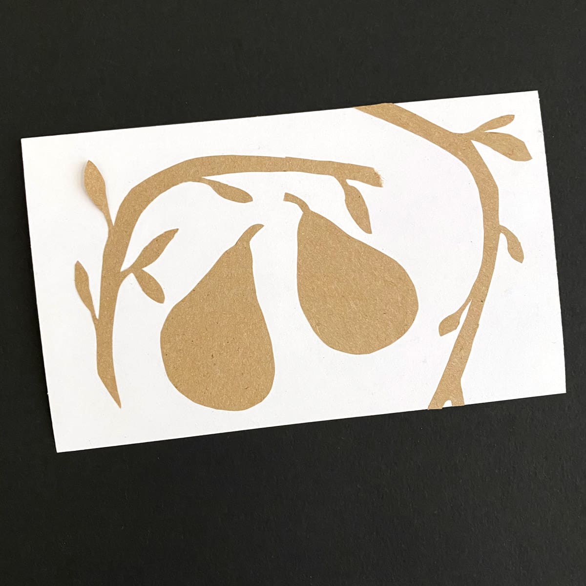 Index card with a Kraft paper silhouette of two pears and pear tree branches on a black background by Mozaic Studio for ICAD 2025