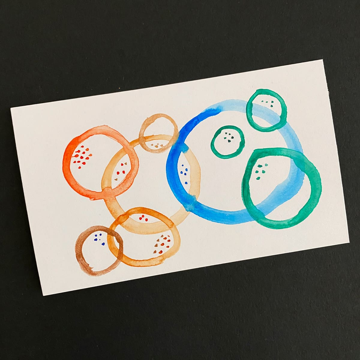 Index card with an abstract watercolor of overlapping circles in bronze, orange, blue and green on a black background by Mozaic Studio for ICAD 2025