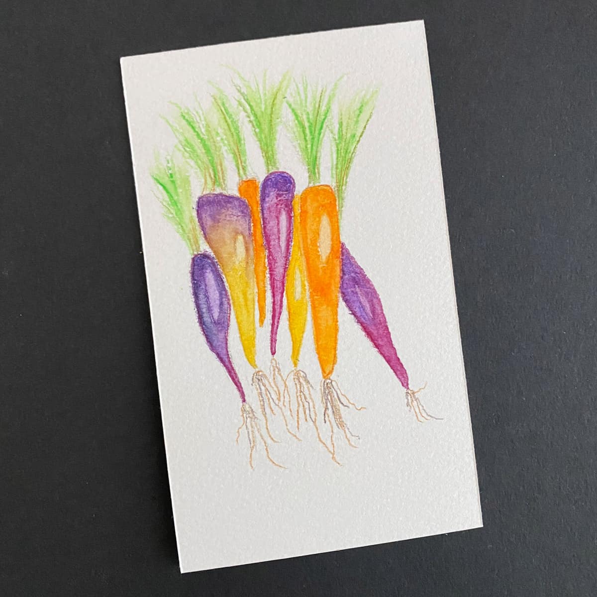 Index card with a watercolor painting of orange, yellow and purple carrots on a black background by Mozaic Studio for ICAD 2025