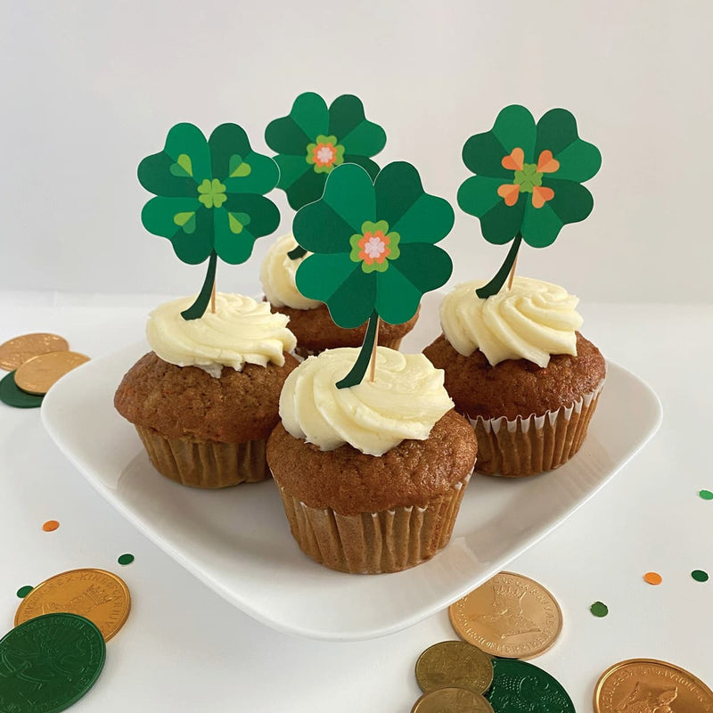 Cupcakes with white frosting and four-leaf clover decorations on a white plate, with gold coins and green leaves in the background.