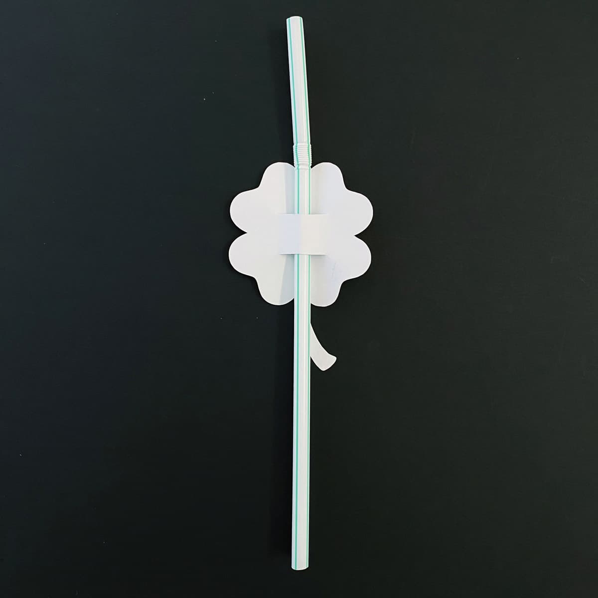 White paper shamrock with a green straw on a black background