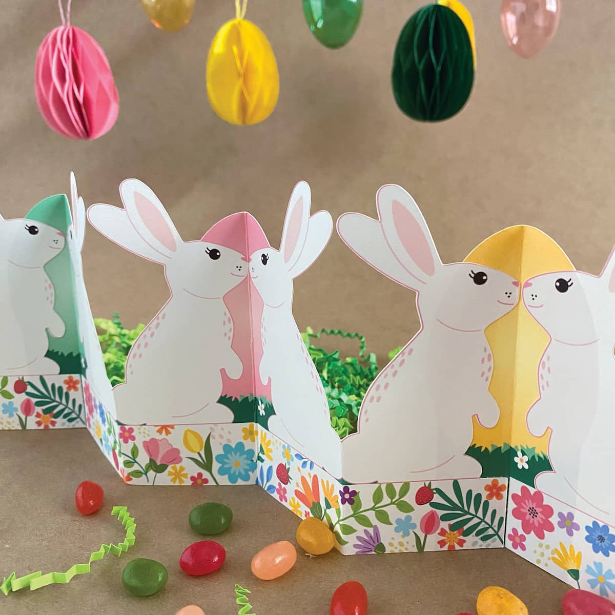 Finished printable standing bunny garland displayed on Easter table with basket, grass, colored eggs, and jelly beans – self-standing accordion fold tabletop decor