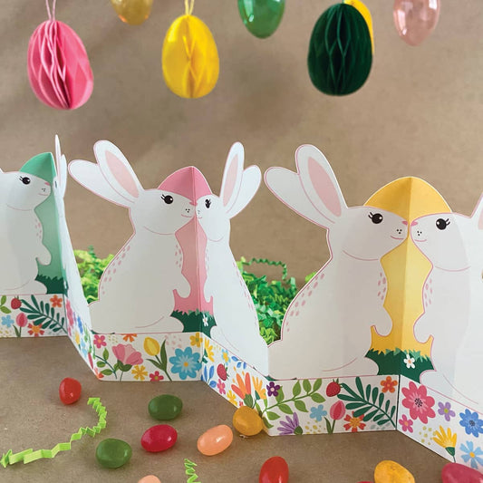 Finished printable standing bunny garland displayed on Easter table with basket, grass, colored eggs, and jelly beans – self-standing accordion fold tabletop decor